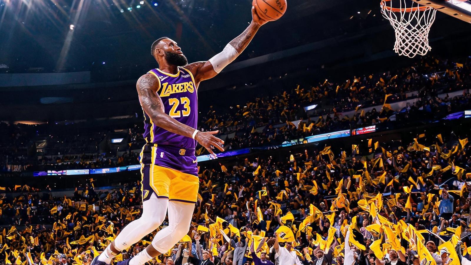 NBA季后赛中湖人队球员突破上篮，球馆内灯光炫目，观众挥动毛巾